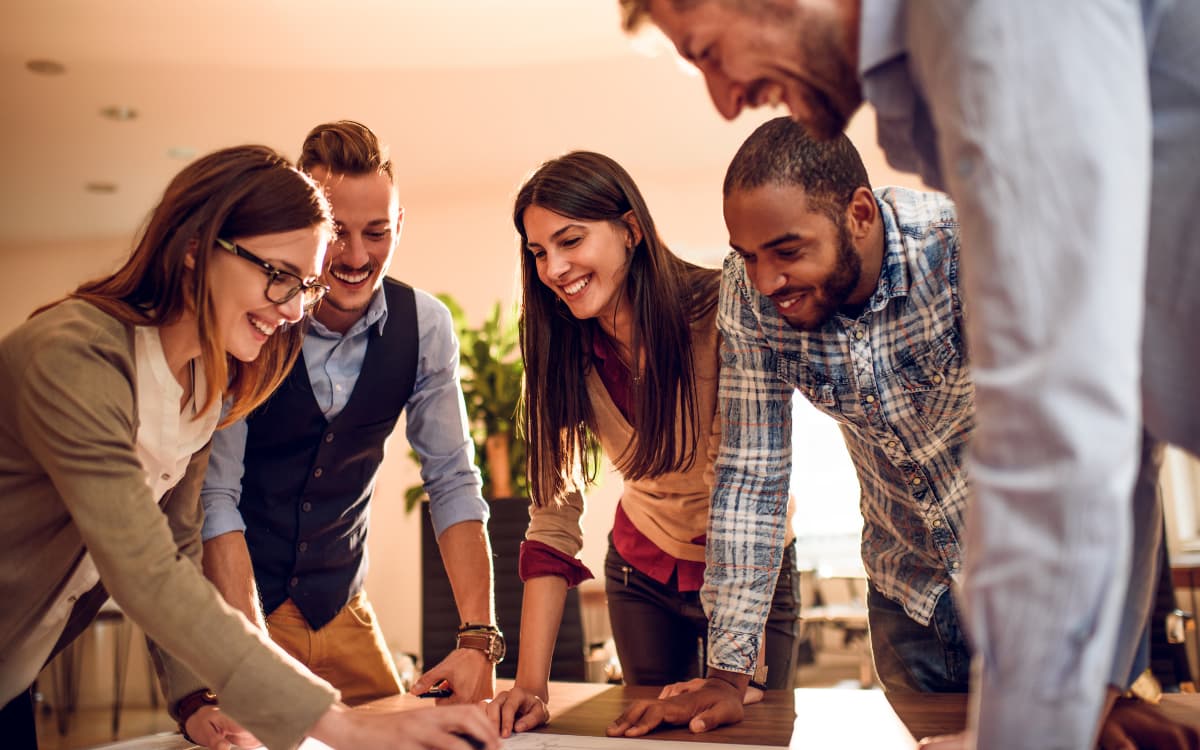 Team of professionals leaning over a desk together, reviewing documents and smiling during a meeting.