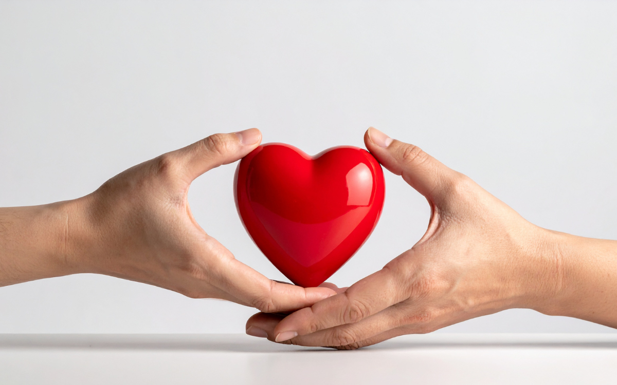 Person passing a red heart symbol into another person’s hands, representing care and support.