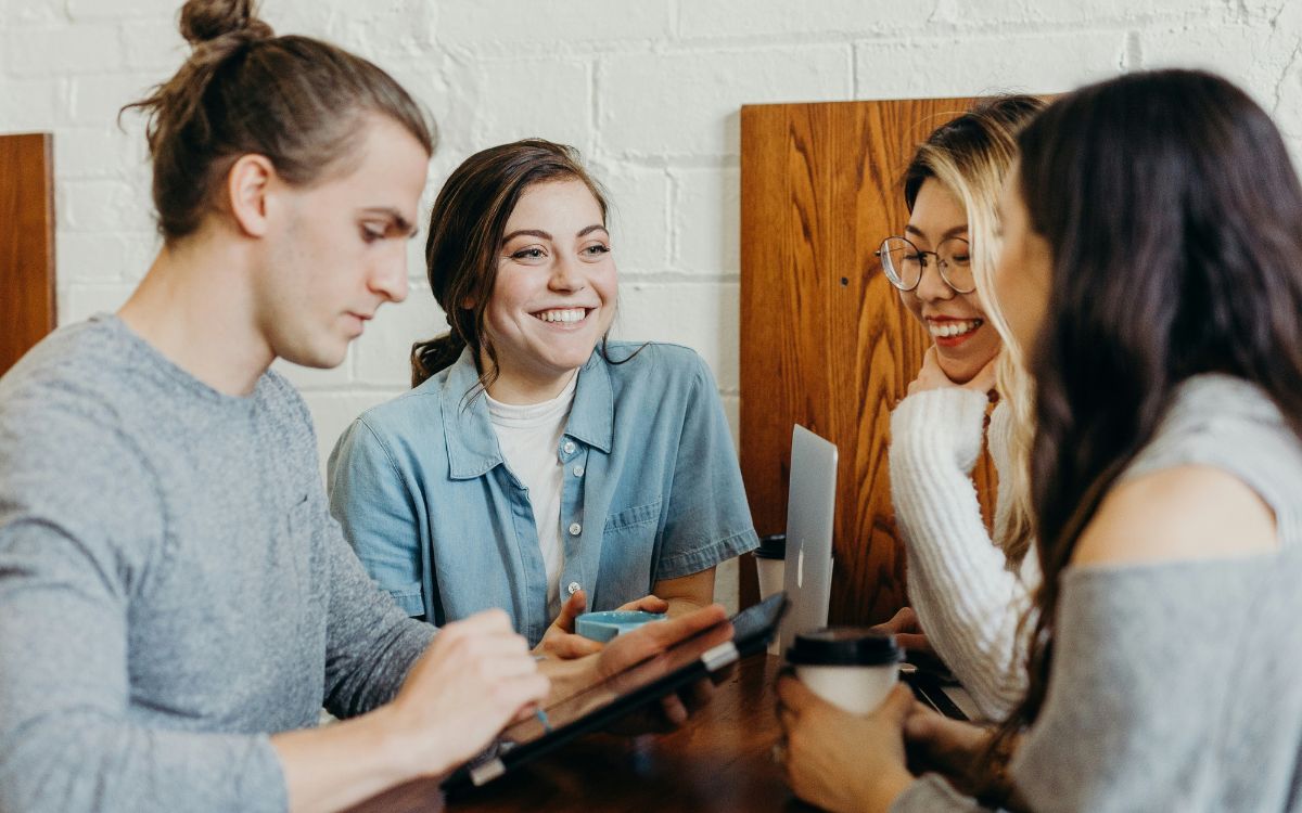 Four people gathered around a table with laptops and notebooks, smiling and collaborating in a casual meeting