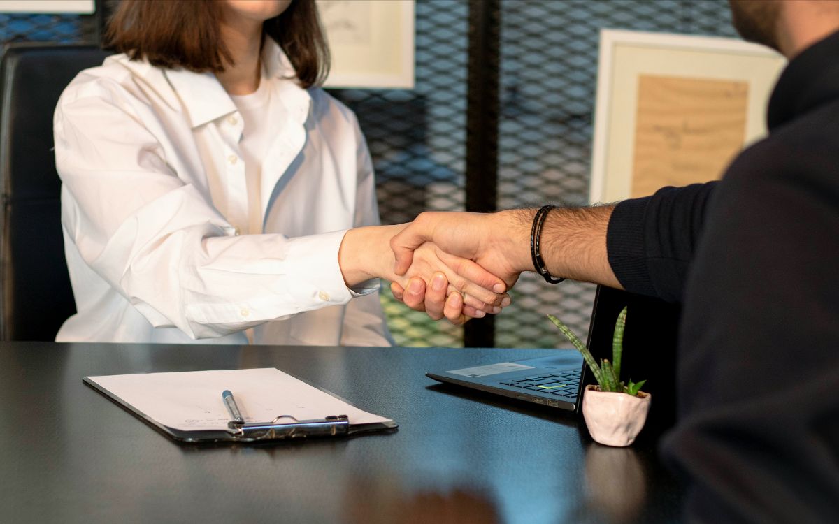 Two people shaking hands across a desk in an office setting