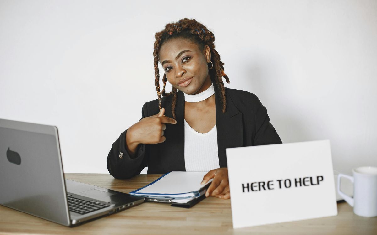 woman sitting at a desk with a here to help sign
