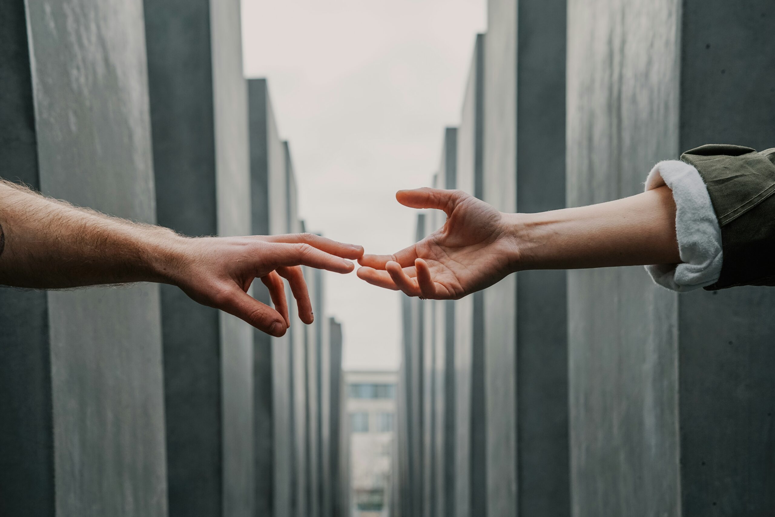 Two hands reaching toward each other between tall concrete structures.